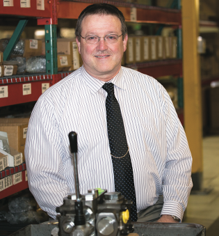 The image shows Brad Smith standing behind a V250 Series valve block in a warehouse.