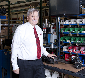 An image of Rick Wallace standing next to a work bench with his hand placed on a rear-mount PTO.