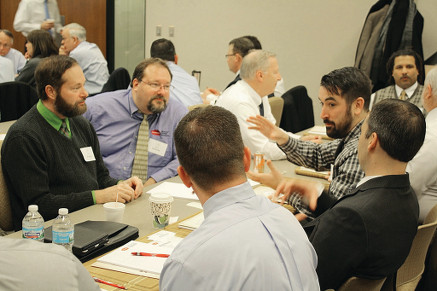 The image shows several people gathered around a table having a discussion.