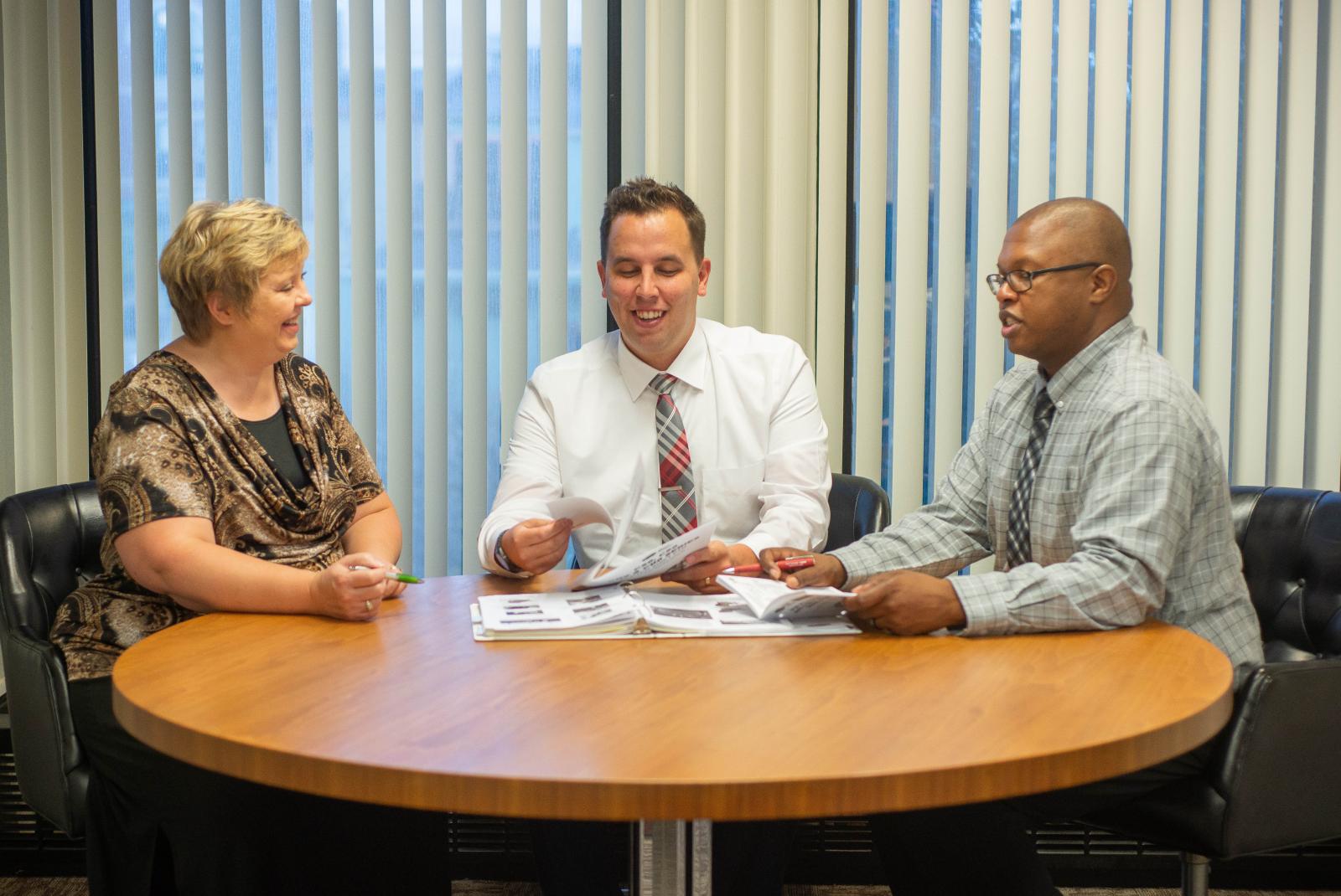 An image of three people sitting at a round table reviewing literature.