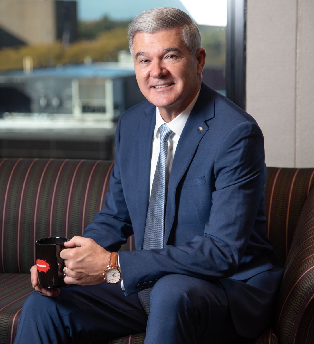 An image of Ray Chambers sitting on a couch holding a Muncie Power mug.